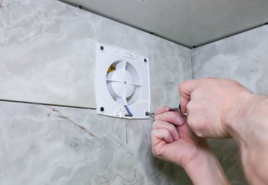 Adam banyo vantilatörünü havalandırıyor. Yenileme işlemi. Tornavida ellerinde..