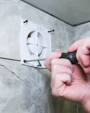 Adam banyo vantilatörünü havalandırıyor. Yenileme işlemi. Tornavida ellerinde..