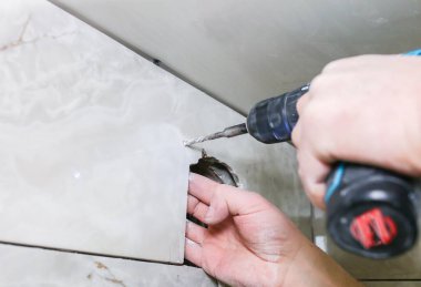 Adam elinde matkap tutuyor. Duvar banyosu vantilatör vantilatörü takan bir işçi. Restorasyon süreci.