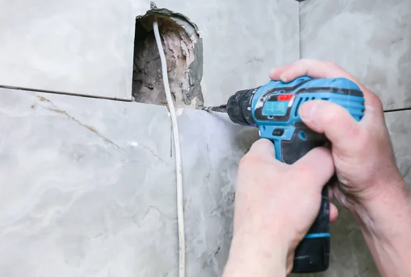 stock image Man is holding hand drill in hands. Worker installing the wall bathroom fan vent. Restoration process.