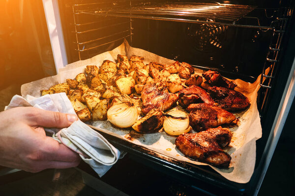 Картофель и курица со специями пекут в электрической духовке.