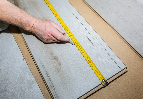 Worker making laminate flooring in apartment. Measure tape and pencil in hands. Maintenance repair renovation. Wooden parquet planks indoors.