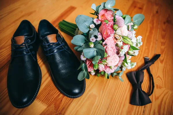 Wedding day accessories. Groom\'s shoes with bouquet on the wooden background. Golden rings and bow tie are nearby. Stylish things.