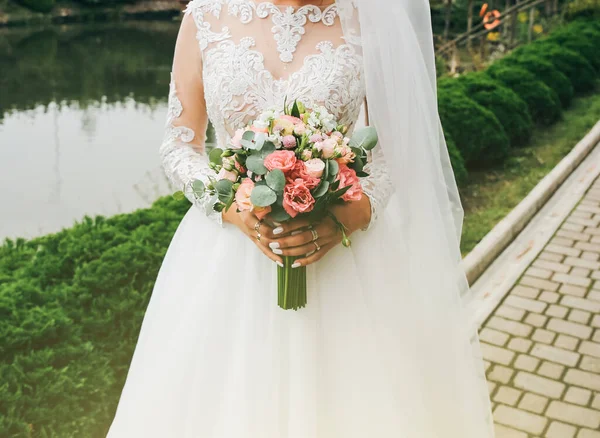 美しい花嫁が花束を手に持っています 屋外で結婚式の写真 袖丈の長い白いドレスと白いレース — ストック写真