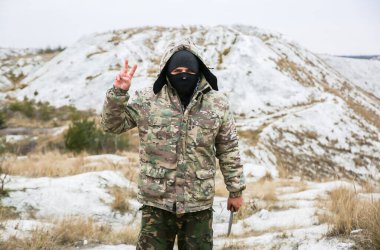 Asker, kamuflaj üniforması ve damalı bandana giyiyor. İnsan, terk edilmiş bir yerde, dışarıda. Huzurlu işaret.
