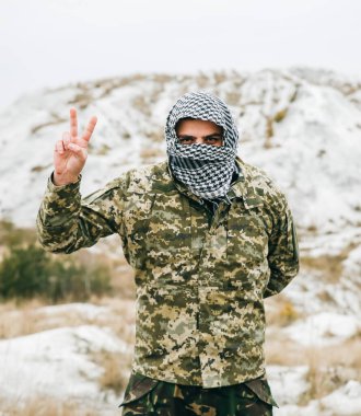 Asker, kamuflaj üniforması ve damalı bandana giyiyor. İnsan, terk edilmiş bir yerde, dışarıda. Huzurlu işaret.