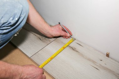 İşçi dairede döşeme kaplaması yapıyor. Mezurayı ve kalemi elinde tut. Onarım onarımı. Ahşap parke kalasları içeride..