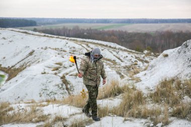 Asker meşaleyi ateşle tutuyor. Kamuflaj üniformalı ve bandanalı bir adam. Dağlarda yaşayan bir adam. Beyaz tepeler ve çöldeki kuru otlar..