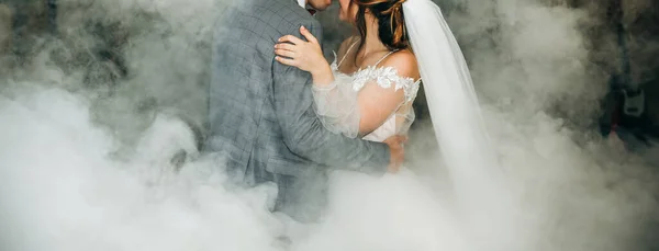 Wedding couple first dance. Bride and groom are hugging. White decorative smoke. Happy emotions. Beautiful long sleeve dress.