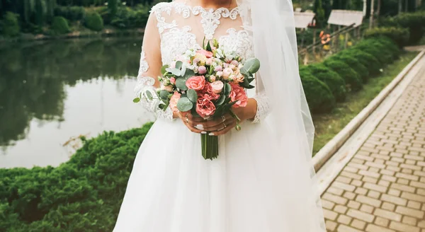 美しい花嫁が花束を手に持っています 屋外で結婚式の写真 袖丈の長い白いドレスと白いレース — ストック写真