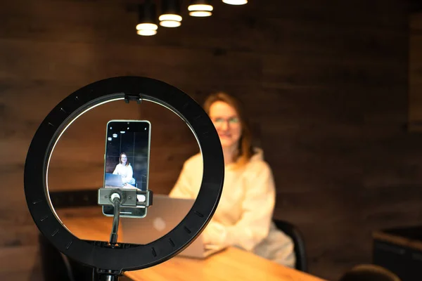 stock image Social media influencer creating content at modern studio sharing online stream using smartphone and laptop. Girl blogger smiling and speaking recording video  with ring lamp. Online training courses.