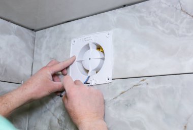 Adam banyodaki vantilatör vantilatörünü takıyor. Yenileme işlemi. Kablolar ellerinde.