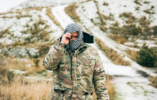 stock image Soldier is standing in the camouflage uniform and checkered keffiyeh shemagh bandana. Binocular in hands. Man is outdoors in the abandoned deserted place.