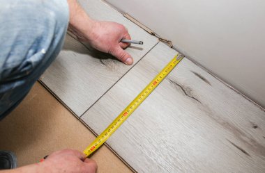 İşçi dairede döşeme kaplaması yapıyor. Mezurayı ve kalemi elinde tut. Onarım onarımı. Ahşap parke kalasları içeride..