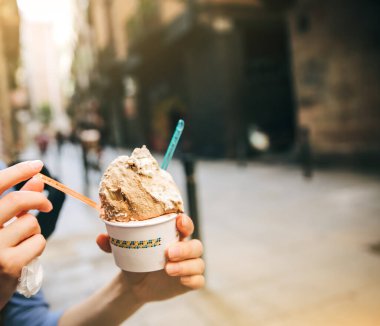 Kız caddede lezzetli dondurmalar yiyor. Plastik kaşık tutan bir kadın. Mükemmel soğuk yaz tatlısı. Yemek fotoğrafı. Tatillerde dinlenmek.