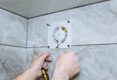 Adam banyo vantilatörünü havalandırıyor. Yenileme işlemi. Tornavida ellerinde..