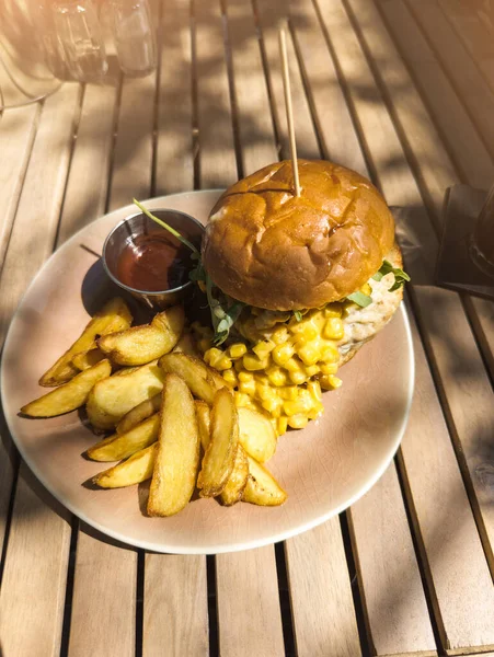 Açık hava restoranındaki masada duran Lezzetli yemeğin dikey fotoğrafı. Patates dilimli hamburger, mısır ve tavuk eti..