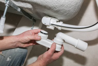 Banyo kurulumu. İşçi hortum borusuyla drenaj yapıyor. Dairede bakım onarımı var. Yenileme işlemi.