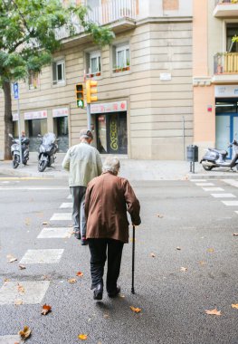 Barcelona, İspanya - 15 Ekim 2018 Barselona 'da trafik ışıklarında karşıdan karşıya geçen yaşlı çift. Sopalı yaşlı adam ve kadın.