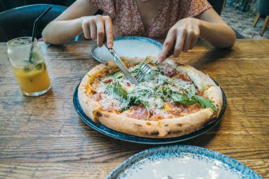 Parmesanlı, roka ve jamonlu İtalyan pizzası yiyen bir kadın..