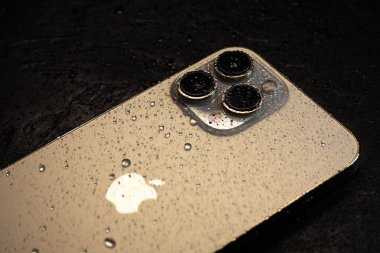 KYIV, UKRAINE - 20 Ekim 2023: Modern akıllı telefon Apple iPhone 15 Pro ve siyah zemin üzerinde su damlaları. Suya dayanıklı modern teknoloji.