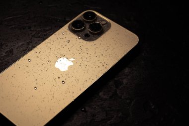 KYIV, UKRAINE - 20 Ekim 2023: Modern akıllı telefon Apple iPhone 15 Pro ve siyah zemin üzerinde su damlaları. Suya dayanıklı modern teknoloji.