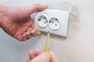 Adam elinde beyaz plastik soketle tornavida tutuyor. Bakım onarımı dairede tadilat yapıyor. Kapalı alanda restorasyon. Elektrik ve ışıklar..