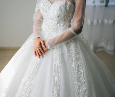 Gelin, lüks uzun kollu elbisesinde altın yüzüklerle el ele tutuşuyor. Güzel tırnaklar. Yapay kristal elmaslar. Düğün mücevherleri..