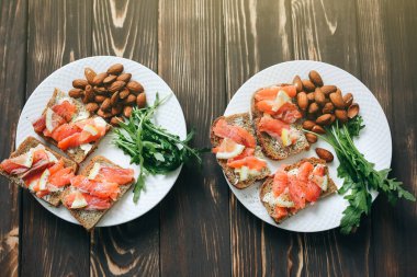 Beyaz tabakta somonlu tam teşekküllü ekmek. Arugula ve limonlu badem. Sağlıklı sandviçler. Atıştırmalık için Omega-3. Düzgün beslenme. Spor yemeği..
