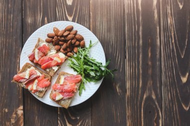 Beyaz tabakta somonlu tam teşekküllü ekmek. Arugula ve limonlu badem. Sağlıklı sandviçler. Atıştırmalık için Omega-3. Düzgün beslenme. Spor yemeği..