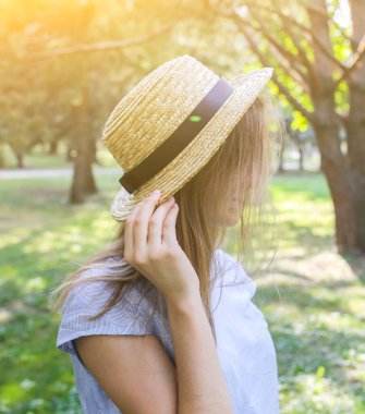 Hasır şapkalı şık hippi kız dışarıda bekliyor. Mavi elbiseli mutlu kadın. Seyahat tatili konsepti. Yaz yaşam tarzı fotoğrafı. Güneşin ve ağaçların gölgeleri.