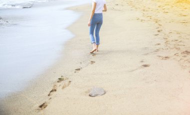 Hippi kız sahilde yürüyor. Deniz manzarası çok güzel. Okyanus kıyısında büyük dalgalar. Sahil şeridinde ayak izleri var. Yaz tatili. Seyahat kavramı.
