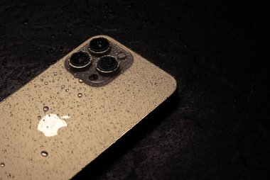 KYIV, UKRAINE - 20 Ekim 2023: Modern akıllı telefon Apple iPhone 15 Pro ve siyah zemin üzerinde su damlaları. Suya dayanıklı modern teknoloji.