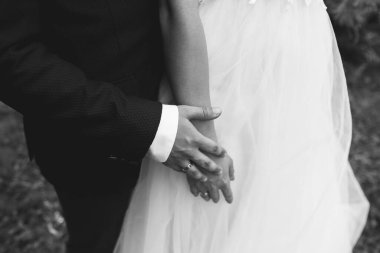 Düğün çifti dışarıda sarılıyor. Gelin ve damat el ele tutuşuyorlar. Aşk hikayesi. Şık kıyafetler..