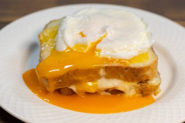 Dilimlenmiş jambonlu ızgara sandviç, erimiş peynir, dijon hardalı ve beşamel soslu haşlanmış yumurta..