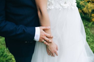 Düğün çifti dışarıda sarılıyor. Gelin ve damat el ele tutuşuyorlar. Aşk hikayesi. Şık kıyafetler..