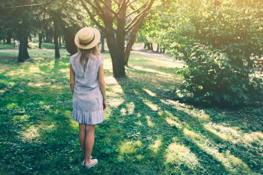 Hasır şapkalı şık hippi kız dışarıda bekliyor. Mavi elbiseli mutlu kadın. Seyahat tatili konsepti. Yaz yaşam tarzı fotoğrafı. Güneşin ve ağaçların gölgeleri.