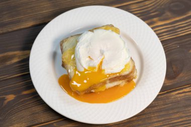 Dilimlenmiş jambonlu ızgara sandviç, erimiş peynir, dijon hardalı ve beşamel soslu haşlanmış yumurta..