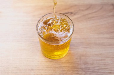 Bir bardağa beyaz köpüklü sıvı altın sarısı bira dökülüyor. Görüntüyü kapat.