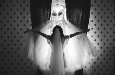 Güzel gelin gelinliğine bakıyor. Kız sabahları kıyafetlerini pencerenin yanında tutuyor..