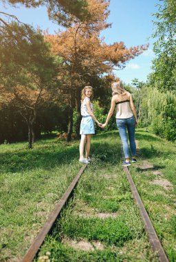 Yeşil parktaki demiryolunda yürüyen iki hippi kız. Aynı cinsiyetten çiftler el ele tutuşuyor. Seyahat tarzı yaşam konsepti. Destek ve dostluk ilişkileri.