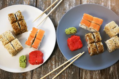 Ahşap arka planda yemek çubukları olan tabaklarda suşi. Japon usulü romantik bir akşam yemeği. Somon, wasabi ve zencefil. Sağlıklı gıda konsepti. Vejetaryen.