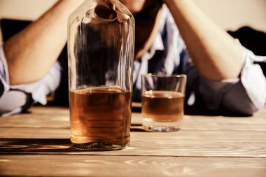 Alkolik bağımlısı. Masanın yanında alkollü ve bardaklı bir adam var. Tehlikeli bir alışkanlık. Sağlıksız yaşam konsepti. Sosyal sorun.