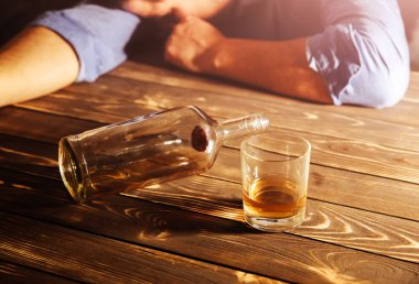 Alkolik bağımlısı. Masanın yanında boş şişesi ve bardağı olan bir adam var. Tehlikeli bir alışkanlık. Sağlıksız yaşam konsepti. Sosyal sorun.