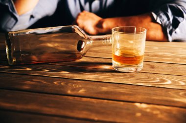 Alkolik bağımlısı. Masanın yanında boş şişesi ve bardağı olan bir adam var. Tehlikeli bir alışkanlık. Sağlıksız yaşam konsepti. Sosyal sorun.
