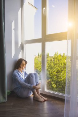 Yerde çıplak ayakla oturan bir kadının dikey fotoğrafı. Evin zemin ısıtma ve akıllı ısıtma kavramı.