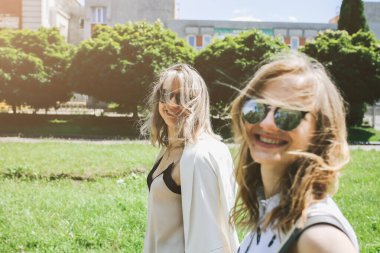 Gözlüklü iki şık hippi kız sokakta yürüyor. Kadınlar için parlak bir yaz fotoğrafı. Güzel kız kardeşler güneşin tadını çıkarıyorlar..