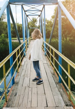 Havalı gözlüklü hippi kız manken fotoğrafı için poz veriyor. Genç, modaya uygun bir kadın köprüde duruyor. Doğada yaz foto çekimleri. Yaşam tarzı kavramı.