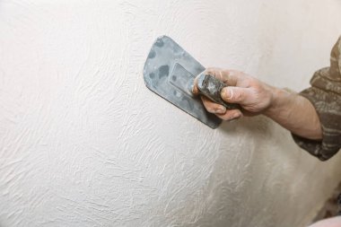 Adam zımpara kağıdıyla bir yüzeyi hazırlıyor. Duvar gıcırtısı. Bakım onarımı dairede tadilat yapıyor. Kapalı alanda restorasyon. Somut arkaplan.