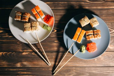 Ahşap arka planda yemek çubukları olan tabaklarda suşi. Japon usulü romantik bir akşam yemeği. Somon, wasabi ve zencefil. Sağlıklı gıda konsepti. Vejetaryen.